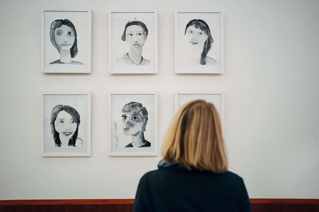 Eine Frau betrachtet Kunstportraits an der Wand in einem Klinikflur