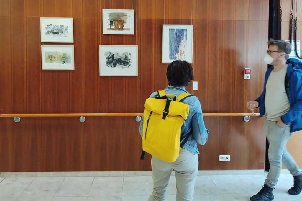 Menschen gehen an einer holzgetäfelten Wand mit Bildern in einem Klinikflur vorbei