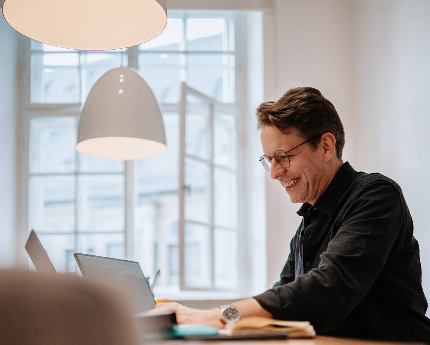 Geschäftsleiter von Remy & Remy arbeitet konzentriert und lachend an mehreren Bildschirmen im Agenturbüro an Projekten für Healthcare-Marketing und Markenentwicklung