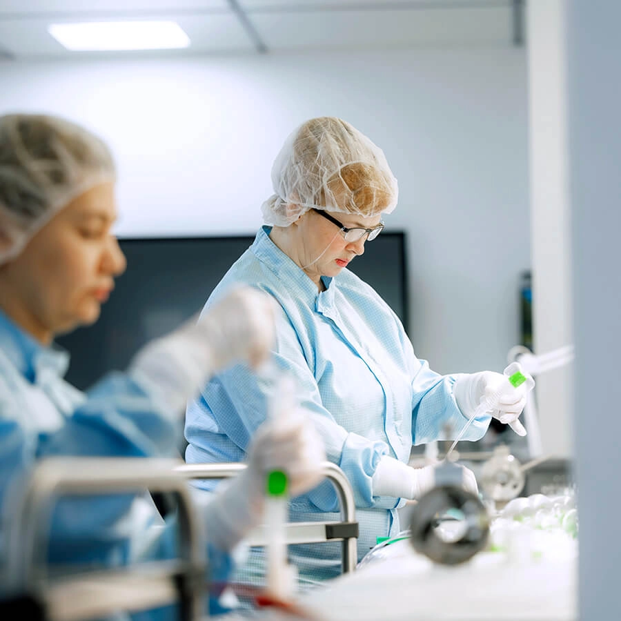 Referenzprojekt Advanced Medical Balloons - Marken-Entwicklung Imagebild - Zwei Laborarbeiterinnen mit hellblauen Kitteln, Schutzbrillen, Haarschutz und Handschuhen arbeiten im Labor.