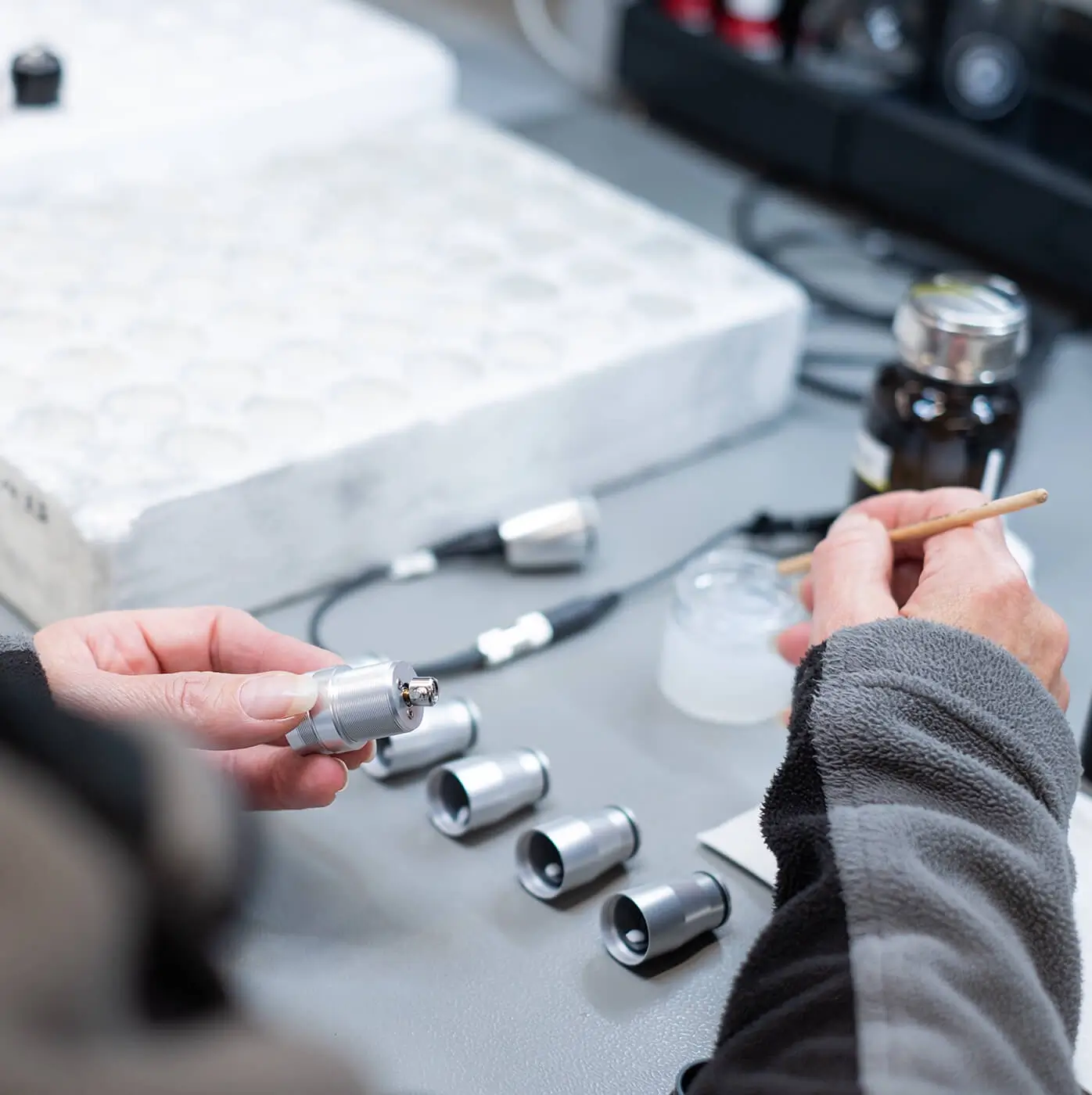 Referenzprojekt Amiea Med - Markenentwicklung und Website Teaserbild mit den Händen einer Person in grauer Jacke, die gerade mit kleinen Metallteilen arbeitet.
