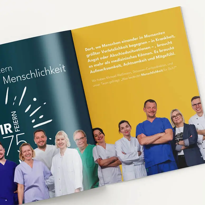 Referenzprojekt Caritas-Krankenhaus St. Josef Jubiläumskampagne Festschrift - Mockup - Innenseiten eines Werbeheftes mit Abbildungen von Ärzten, Pflegekräften und weiteren Mitarbeitern. Die linke Seite ist dunkelblau und zeigt groß das Kampagnenlogo. Die rechte Seite ist gelb und enthält Informationen.
