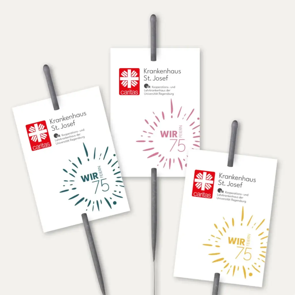 Referenzprojekt Caritas-Krankenhaus St. Josef Jubiläumskampagne Giveaway - Wunderkerzen mit weißen Werbeschildchen, auf denen das Caritas-Logo und das Kampagnenlogo zu sehen sind.