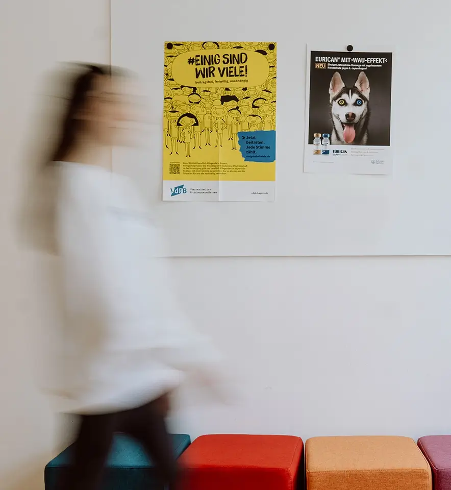 Remy & Remy Mitarbeiterin läuft sehr schnell an einer Wand mit Kreativboard an dem Arbeitsbeispiele zu sehen sind und bunten Besprechungshockern vorbei