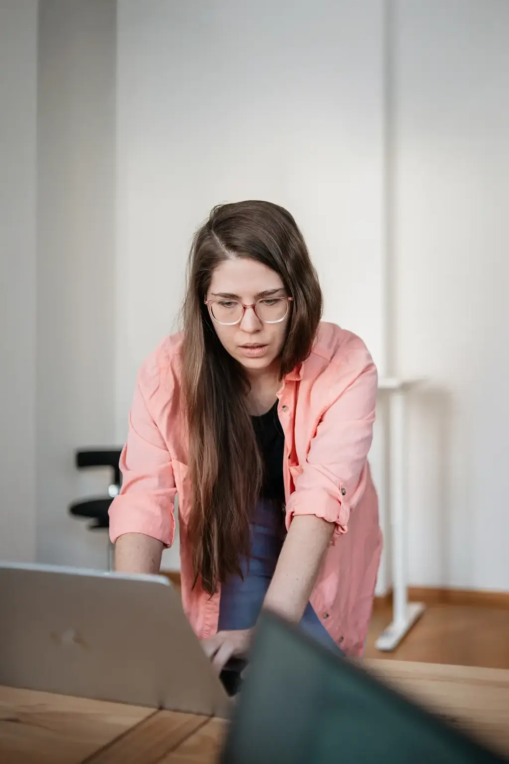 Junge Remy&Remy Mitarbeiterin mit langen Haaren Brille und rosa Bluse blickt konzentriert auf Ihren Laptop