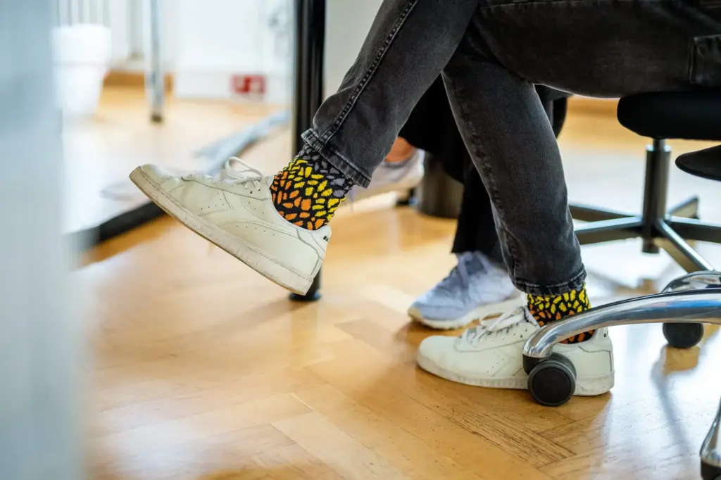 Bunte Socken eines Mitarbeiters von Remy & Remy im Büro am Schreibtisch als Ausdruck der kreativen Unternehmenskultur einer Agentur für Healthcare-Kommunikation und Markenentwicklung.