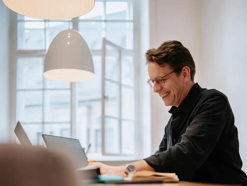 Geschäftsführer in schwarzen Hemd und Brille, konzentriert am Laptop arbeitend, in den hellen Büroräumen von Remy&Remy Healthcare- Kommunikation