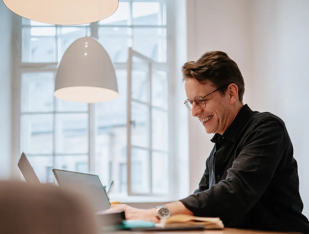 Geschäftsführer in schwarzen Hemd und Brille, konzentriert am Laptop arbeitend, in den hellen Büroräumen von Remy & Remy Healthcare- Kommunikation