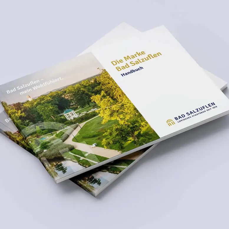 Referenzprojekt Bad Salzuflen Corporate Design - Mockup in Form eines Handbuchs. Auf der linken Seite des Deckblatts befindet sich ein Bild vom Kurpark Bad Salzuflen, mit bunter Natur, großen Bäumen, gepflegten Rasenflächen, Wasserstelle, kleinem Häuschen und Sitzmöglichkeiten. Auf der rechten Seite ist eine weiße Fläche, auf der unten das Logo gedruckt ist und oben bis mittig ein Werbespruch.
