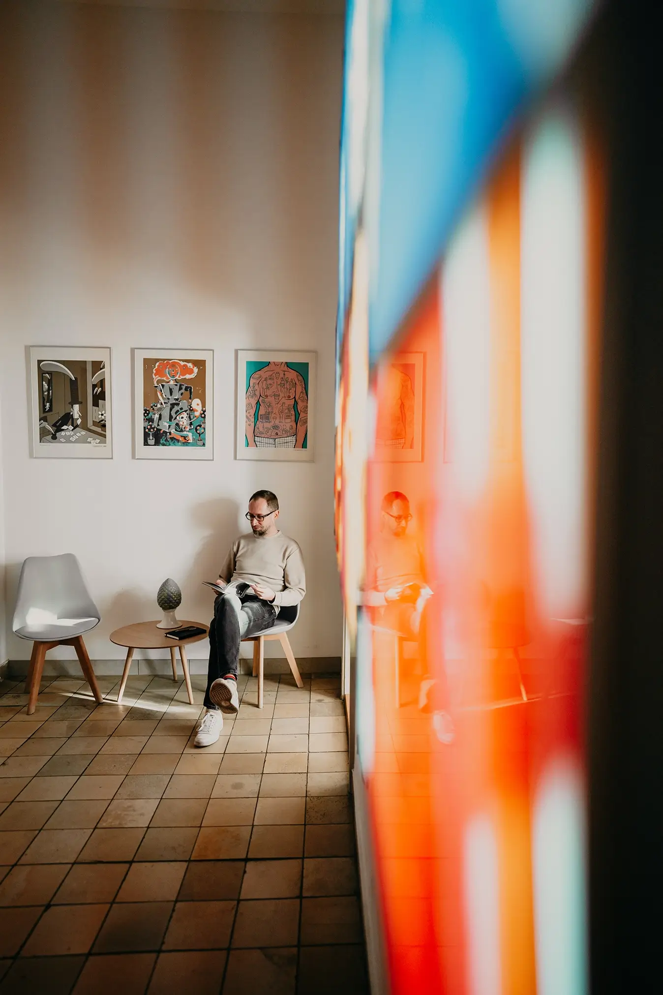Designer der Remy & Remy Agentur, mit Brille, hellem sweatshirt und Jeans liest sitzend ein Fachmagazin in einer hellen Büroumgebung und informiert sich zu Themen der Healthcare-Kommunikation, Medical Writing und strategischen Markenführung. Der Raum ist durch die Bilder über ihm bunt und krativ gestalltet.
